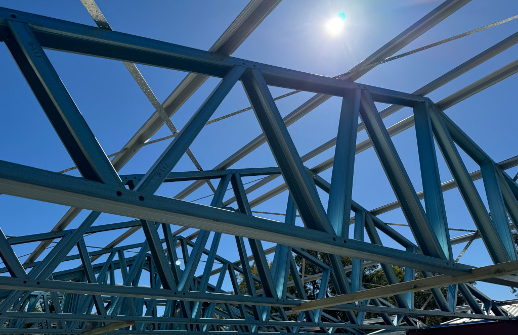 Steel roof trusses viewed from below against a bright sky